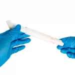 Two hands wearing blue gloves hold a white laboratory tube against a white background, suggesting a medical or lab setting.CHG Applicator (3mL, 6mL & 10.5mL)